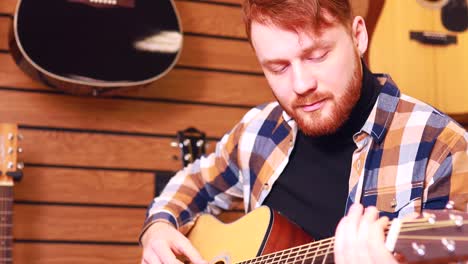 irishman redhaired bearded handsome man in brown plaid casual shirt choosing a guitar in a music store