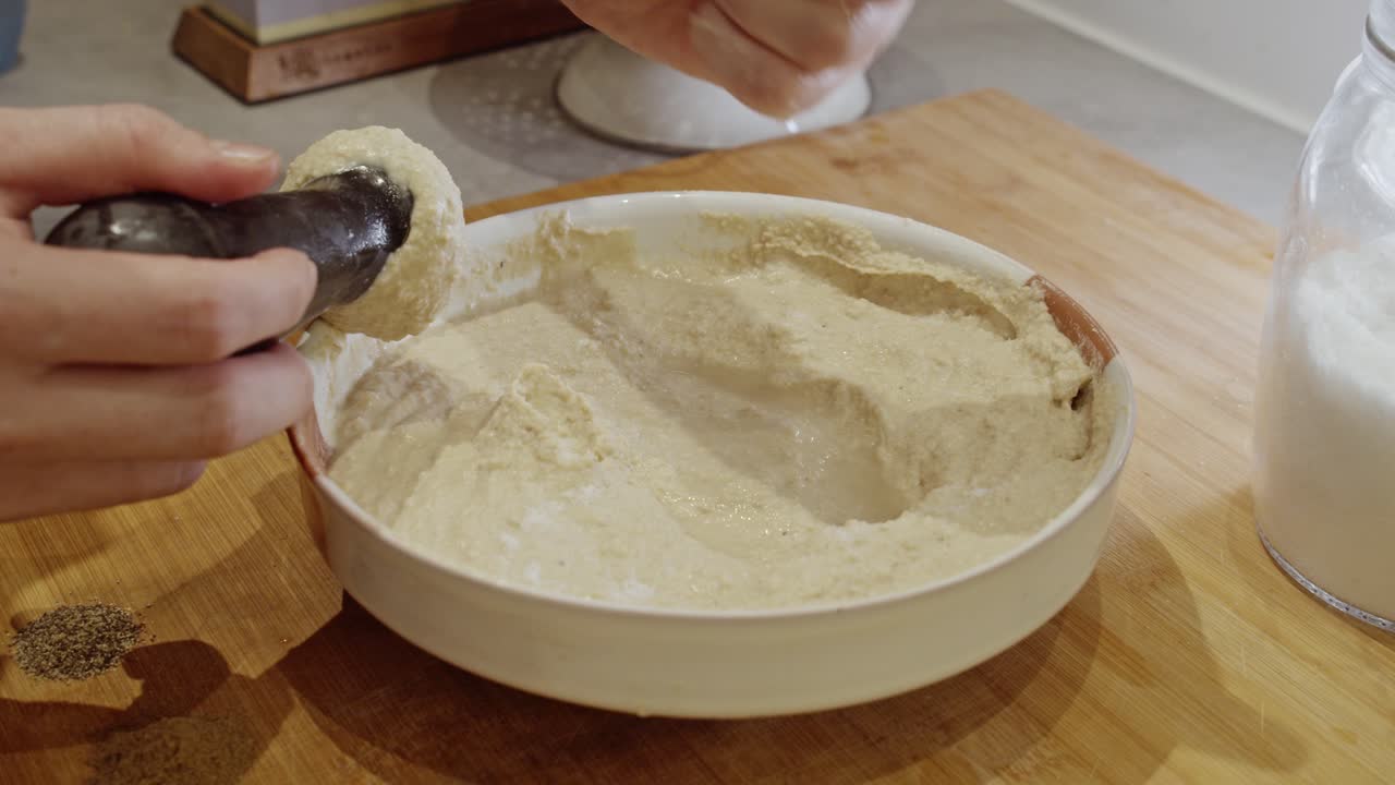 Hand mashing chickpeas into hummus on wooden table in the kitchen