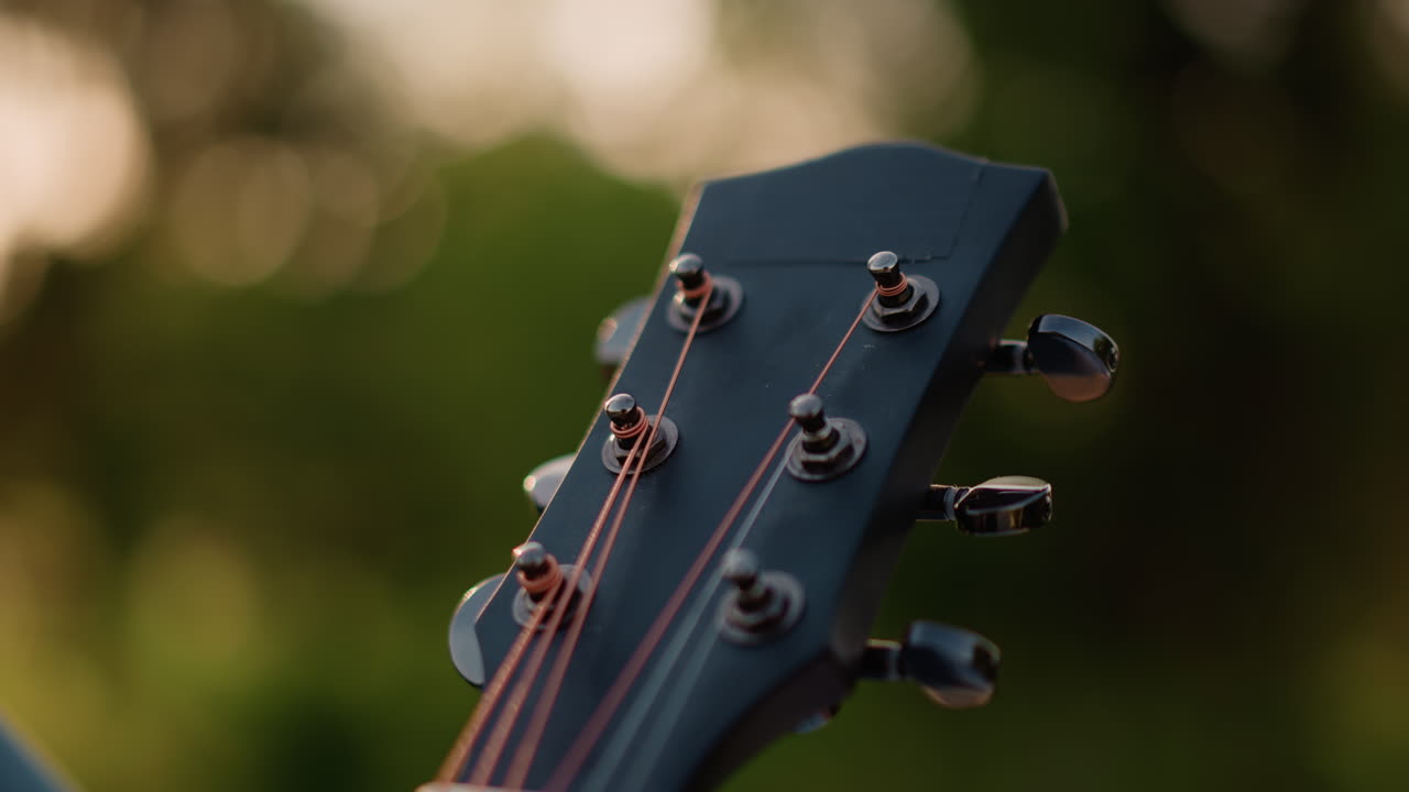 closeup acoustic guitar headstock golden hour warm bokeh background copper strings tuning pegs turning songwriter tuning instrument before sunset performance rustic backyard atmosphere soft golden