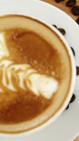 primer plano de una taza de café con platillo y granos de café