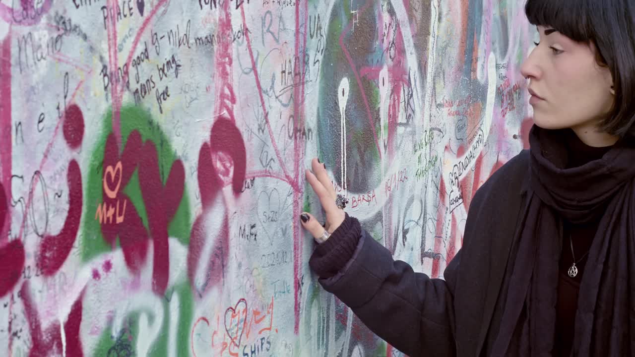 En ung ekstravagant kvinde går langsomt forbi beskederne på Lennonmuren i Prag og læser dem omhyggeligt