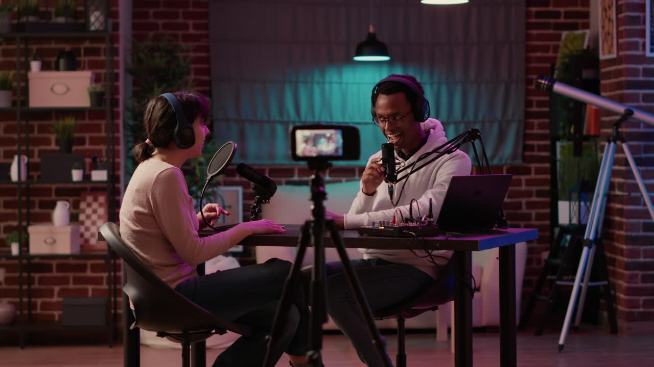 African american online radio host recording vlog using digital camera on tripod and intruducing guest to listeners