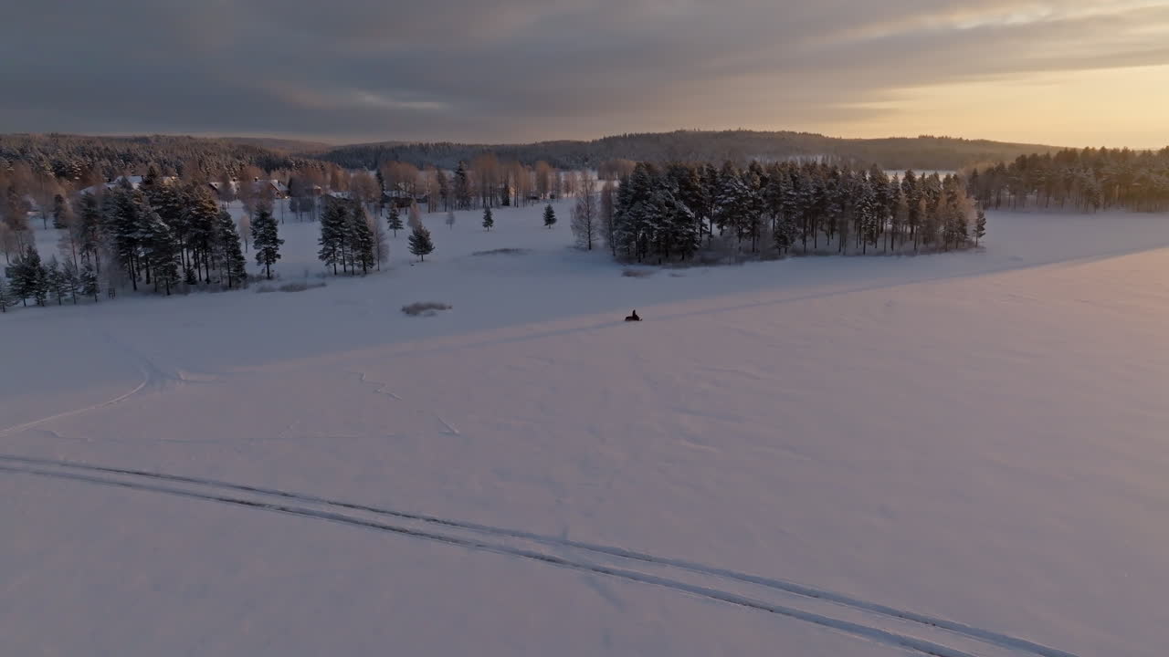 Vista aerea che segue una motoslitta che guida sul ghiaccio, in una fredda mattina d'inverno in Lapponia.