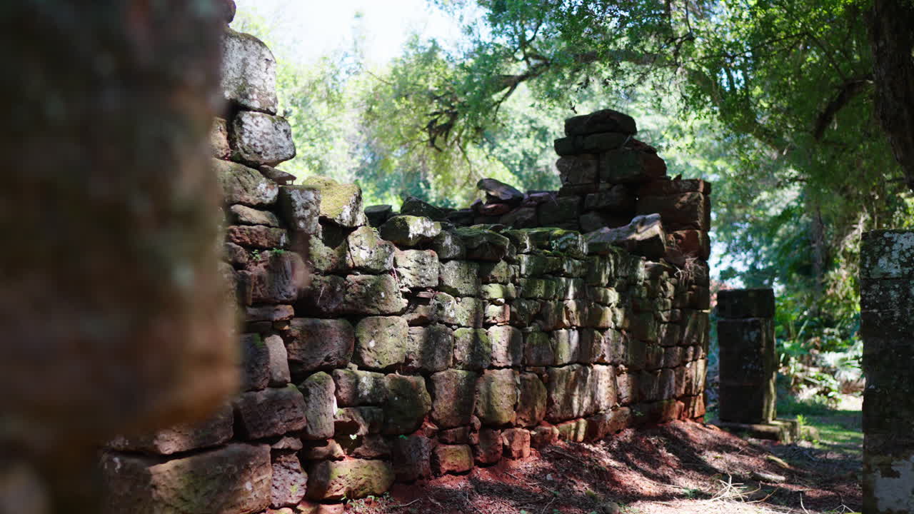 Sunlight filtering through trees illuminates the weathered stone wall, a testament to the passage of time and the enduring legacy of San Ignacio Miní, Misiones, Argentina, slow motion reveal shot