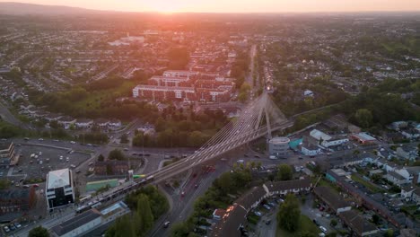 aerial reverse dolly view of a train passing above a cable stayed bridge in dundrum village - south side of dublin during a beautiful and gold sunset - end of summer in ireland