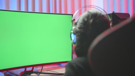 young gamer girl seating on the chair with  green screen computer while playing game