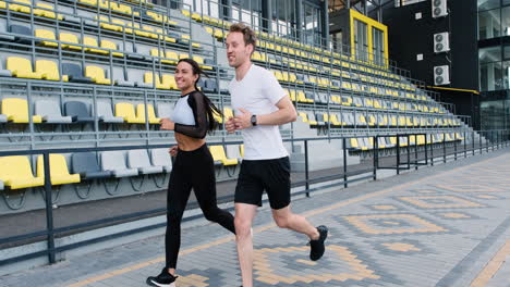 Feliz-Pareja-Deportiva-Hablando-Y-Corriendo-Juntos-En-El-Estadio