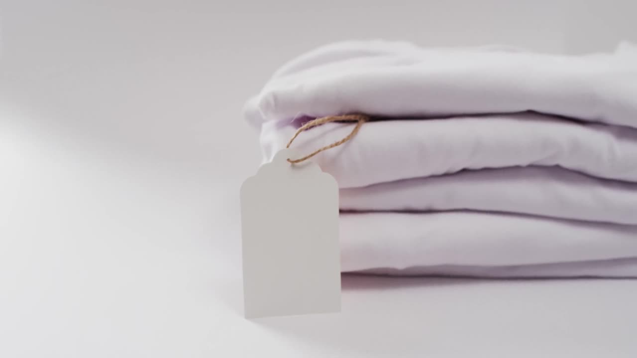 Video of stack of folded white t shirts with copy space on white background
