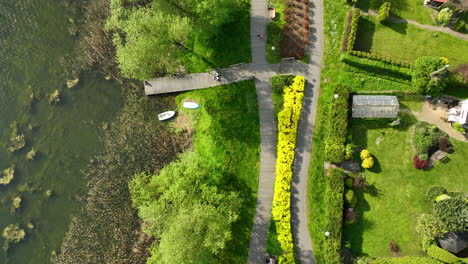 a top-down aerial view of a lakeside area with a dock, boats, and pathways surrounded by greenery