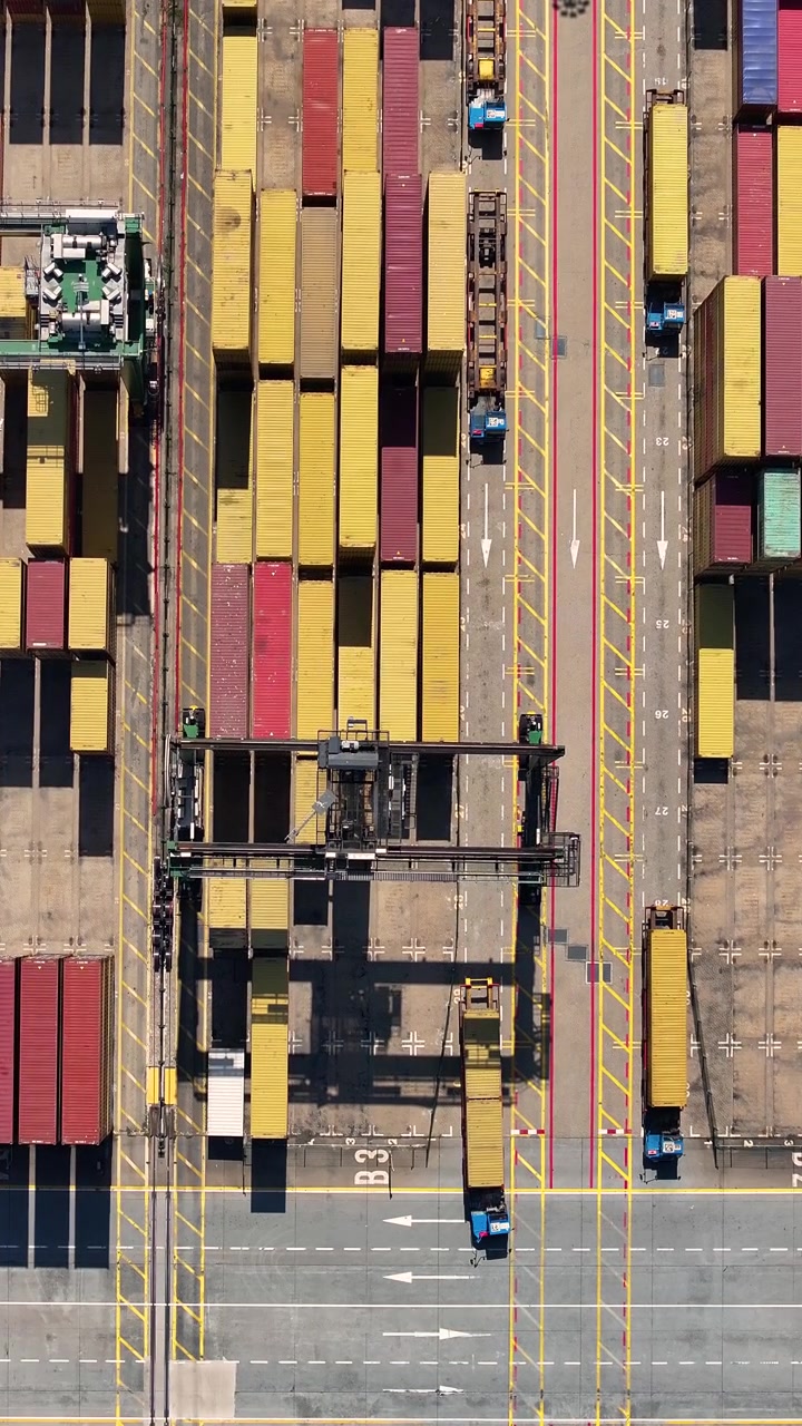 A container terminal with multiple shipping containers arranged systematically. Cargo trucks move in and out, demonstrating freight transportation processes.