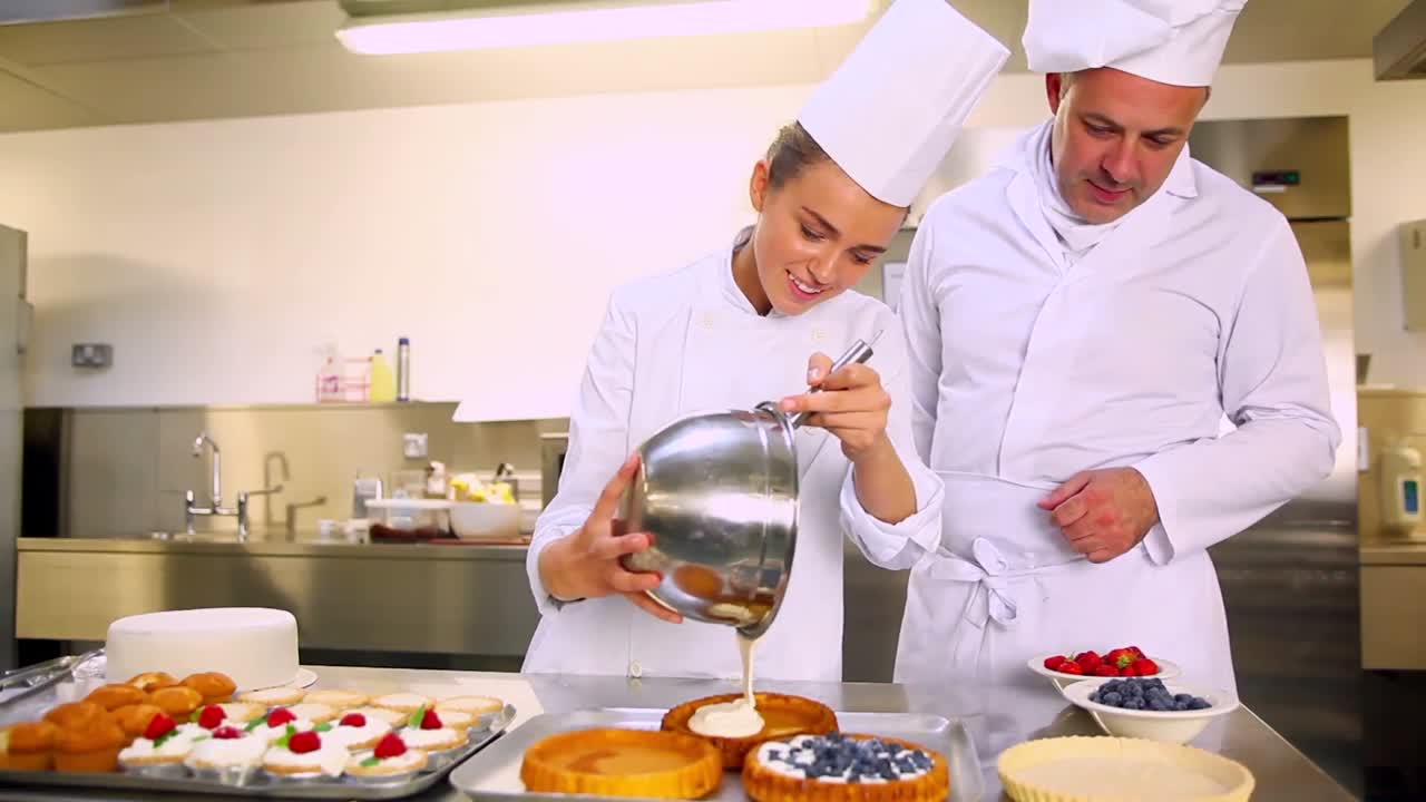 jefe de cocina viendo a su estudiante verter crema en el caso de pastelería