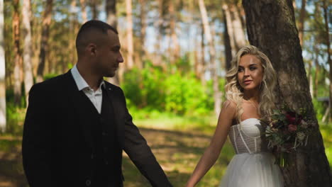 cute newlywed couple walks joining hands along green park