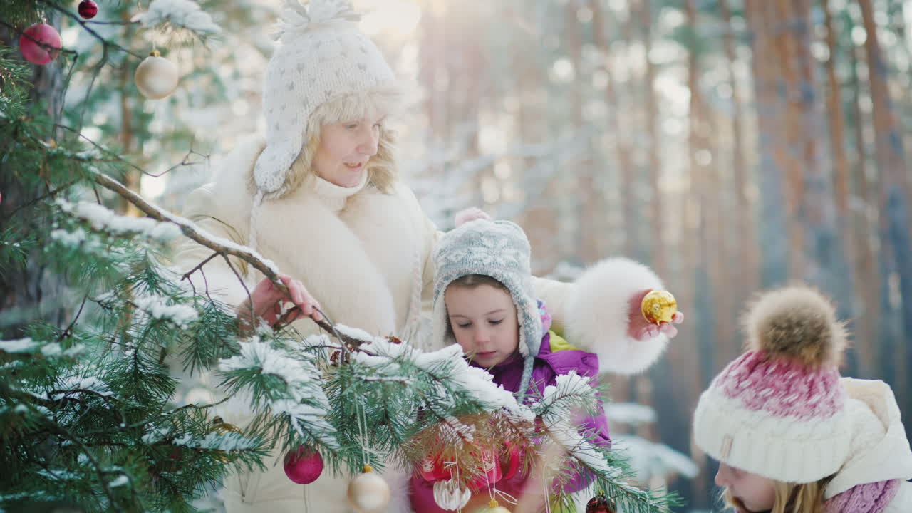 мама с двумя маленькими девочками готовится к рождеству и украшает новогоднюю елку круглыми шарами в с