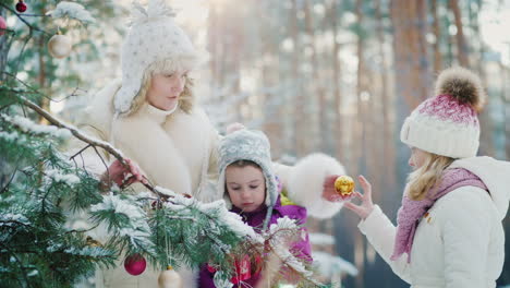 mamá con dos niñas que se preparan para la navidad decoran el árbol de año nuevo con bolas redondas como