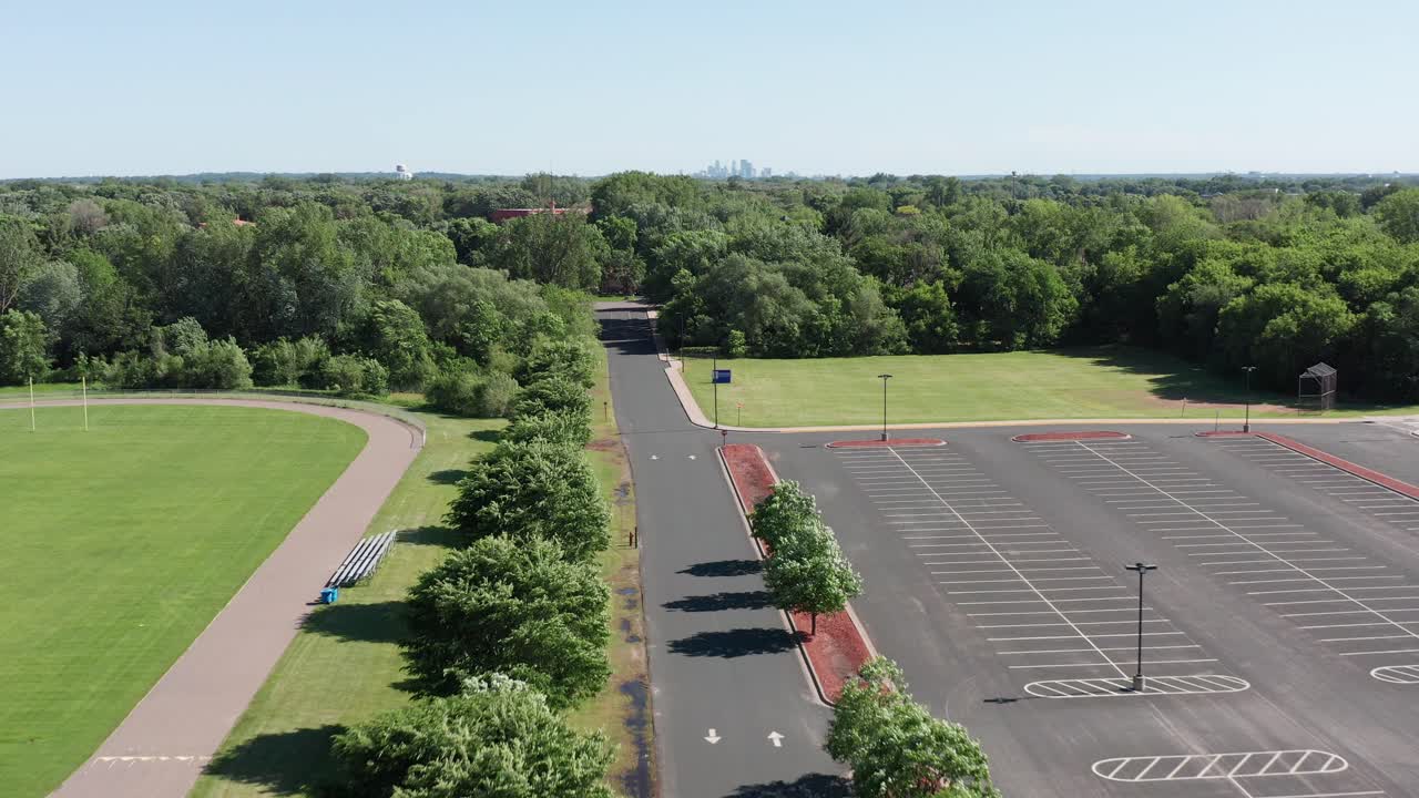 Nedadgående luftoptagelse over en skoleparkeringsplads og atletikbane med Minneapolis' skyline i baggrunden