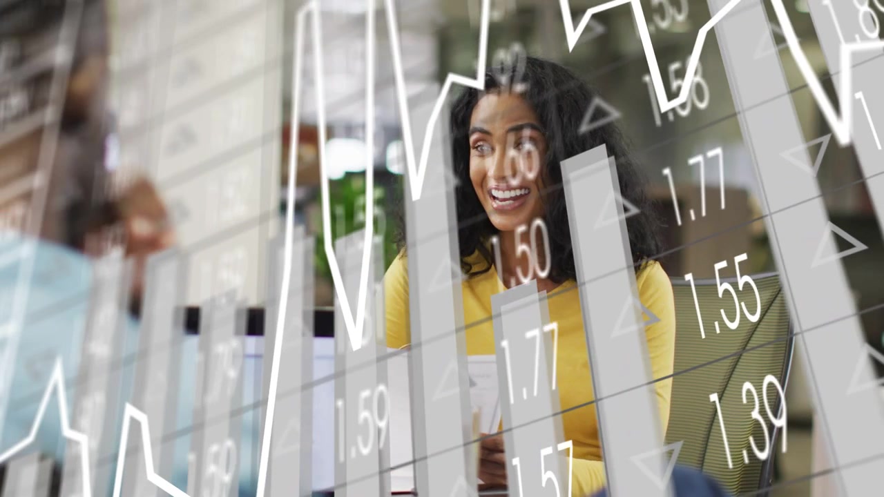 Kvinde i gul beklædning gennemgår finansielle dokumenter, mens en kollega på en bærbar computer får grafer til at skifte til søjlediagrammer.