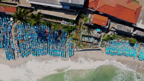 ae4rial top down shot showing crowd of blue colored boats on indonesian beach during summer - waves reaching sandy beach