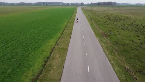 Drone-shot-of-guy-riding-motorcycle-down-a-farm-road-towards-camera