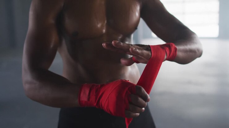 Uomo afroamericano a petto nudo che si fascia le mani per la boxe in un edificio urbano vuoto.