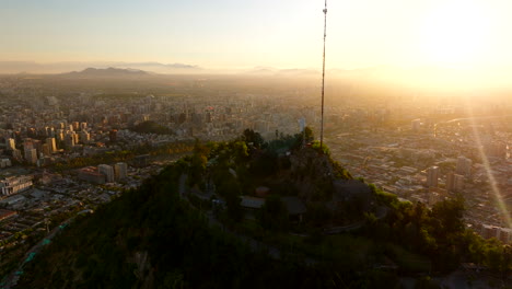 cerro san cristóbal overlooking santiago cityscape, golden hour sunset with sun flare, chile. aerial forward, approach