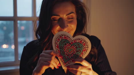 smiling woman holding a decorative heart in warm light