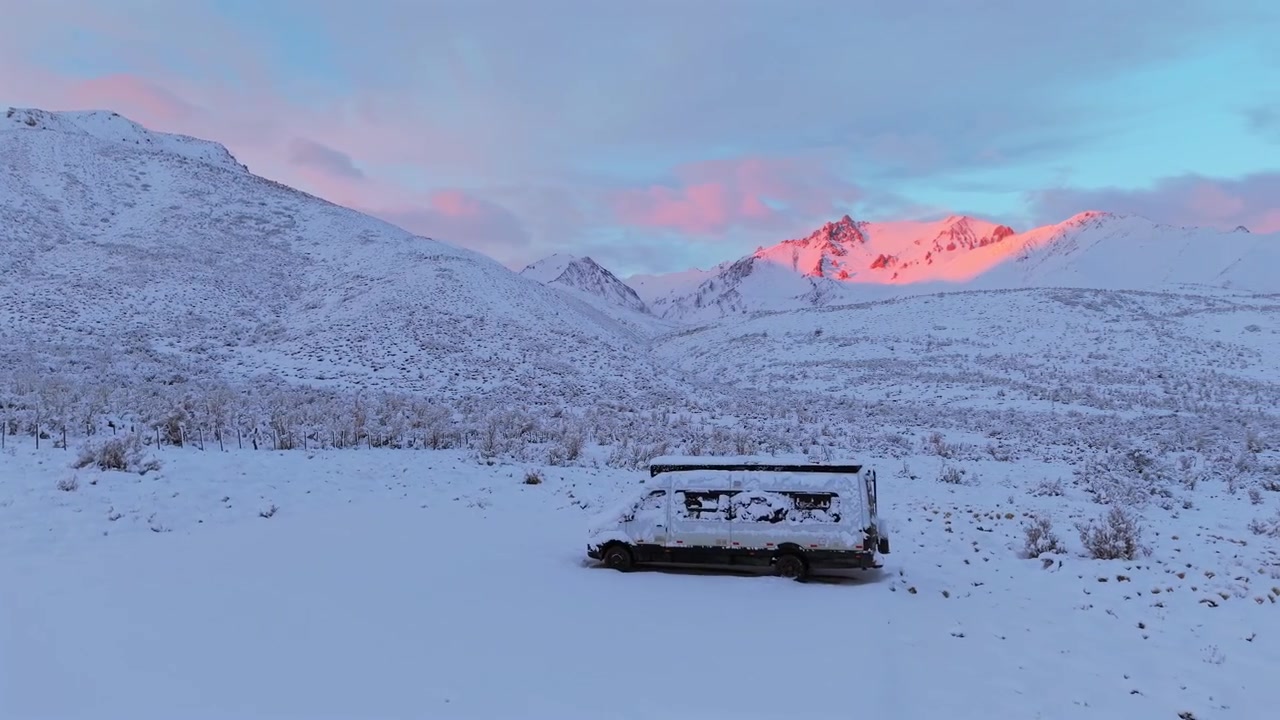 Snow covered camper van parked in remote Andean wilderness in Mendoza, Argentina representing van life, winter camping and overland travel lifestyle beneath sunrise mountain peaks, drone forward dolly