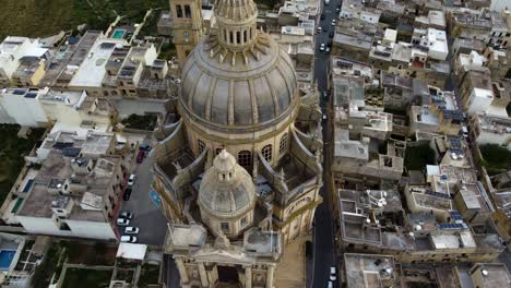 basilica-church-of-Roman-Catholic-parish-church,-Symbolic-to-holy-mother-Mary,-religious-built-sacret-architecture,-dome-with-cross-symbol-on-top,-tilt-up-aerial-drone-movement,-shot-in-malta