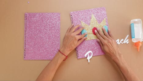 assembling parts of notebook cover with pink glitter background, overhead view