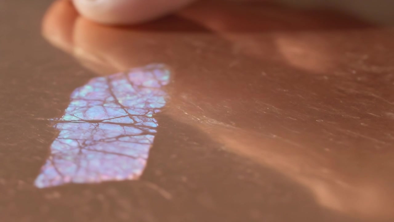 Entering fingertip from right revealing iridescent film on copper tabletop, inspecting vein pattern