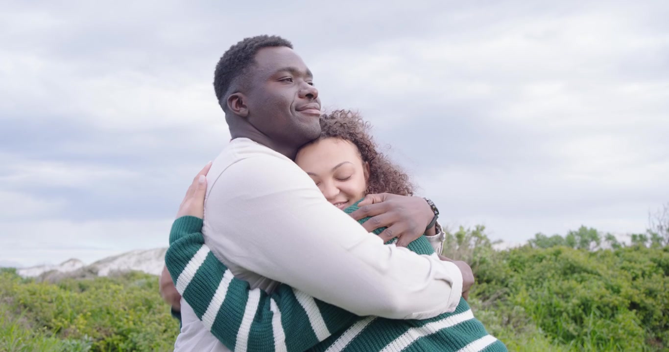 African American couple walking coastal path, man pointing at sea, causing woman gazing and hugging