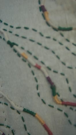 A detailed close-up of multicolored embroidery on light fabric, showcasing intricate hand-stitched patterns