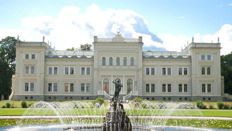 main entrance of oginskis manor with fountain on sunny day with fluffy clouds