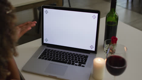 mixed race woman having a romantic dinner blowing kisses on video chat at home