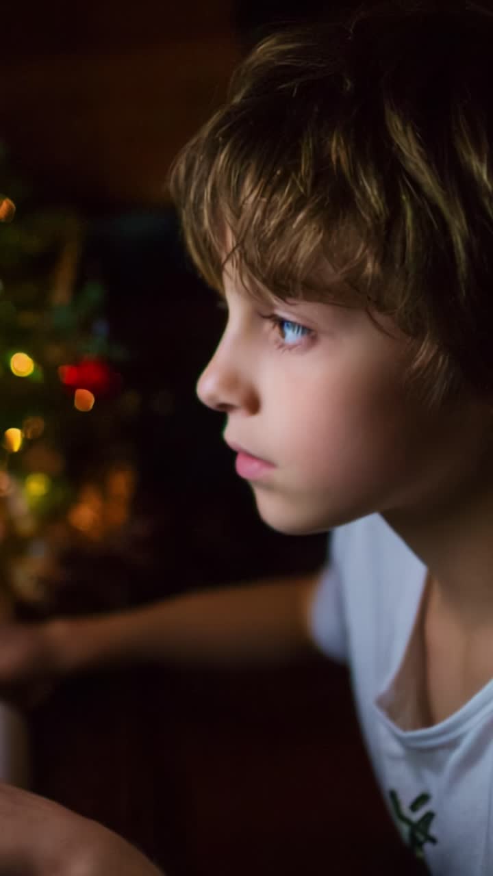 A Focused Child Gazing Carefully at a Screen, Illuminated by a Nearby Christmas Tree, Capturing the Magic of Imagination and Wonder in an Intimate Evening Setting