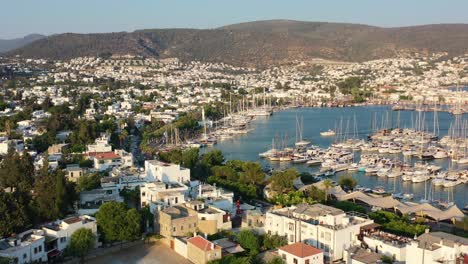 aerial drone flying over bodrum marina full of sailboats on a summer afternoon with the sun setting over the hills and white villas of mugla turkey