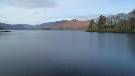 low aerial drone shot over derwentwater lake keswick with derwent island on the right and catbells fell in background on sunny and cloudy morning lake district cumbria united kingdom