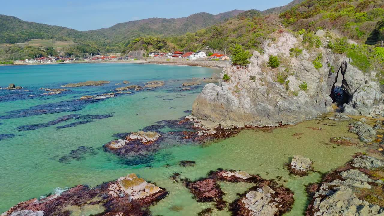 A stunning aerial shot drifts sideways along the picturesque Coast.The camera glides past a large rock formation with sea arch, showcasing the crystal-clear turquoise water and the vibrant reef below