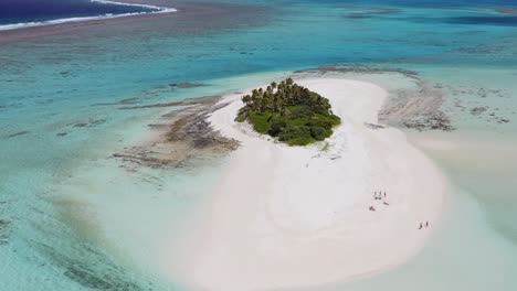 aerial pull back over small sandy island with palm trees to pan up reveal of expansive blue, shallow reef in tonga