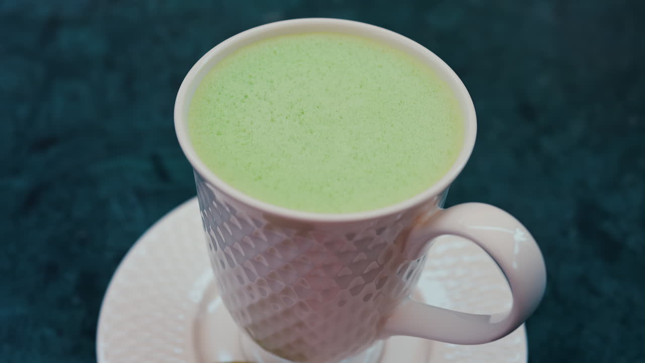 Close up of a smooth matcha latte with vibrant green foam in a white cup