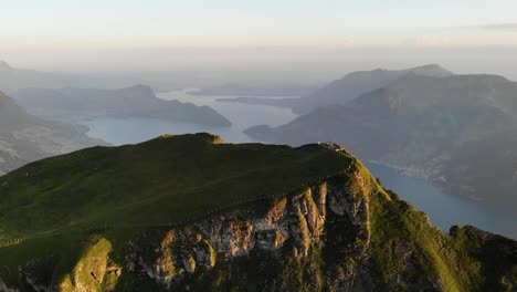 aerial view of niederbauen chulm in uri, switzerland with view of the peak's cliffs and lake lucerne, burgenstock, pilatus plus rigi in the background on a golden summer morning in the swiss alps