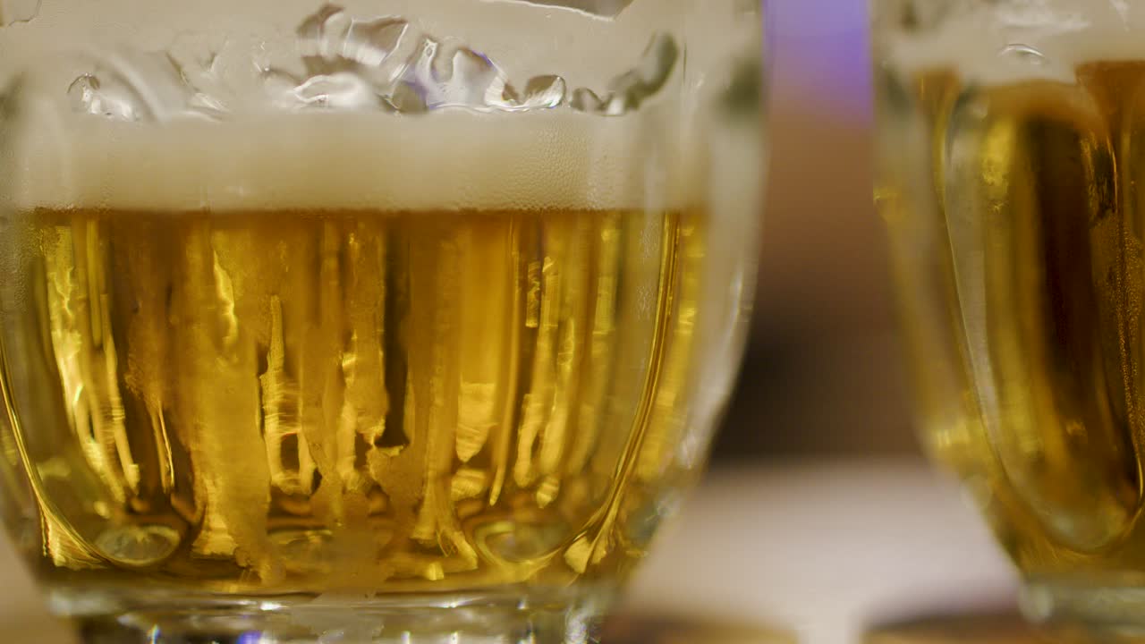 Golden beer poured into glass mug, forming thick foam, under warm ambient bar lighting, close-up