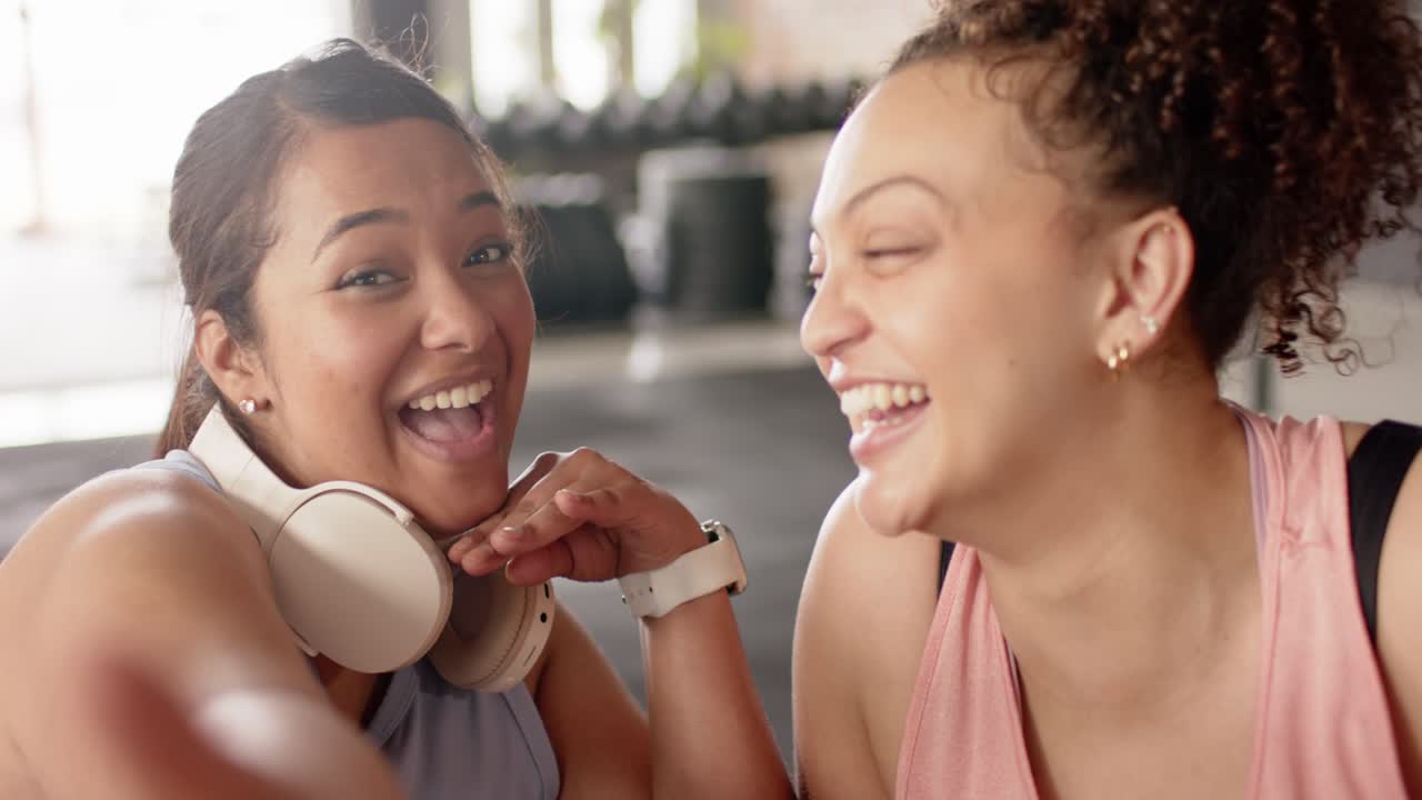 Diverse amiche che sorridono in palestra dopo un bisbiglio, condividendo risate vicino ai porta manubri
