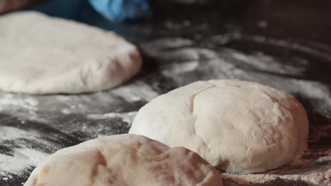 A baker wearing blue gloves prepares and shapes individual dough portions on a floured surface