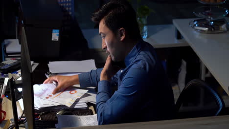 young businessman feeling overwhelmed by a mountain of paperwork. he is feeling stressed and frustrated as he looks at computer screen