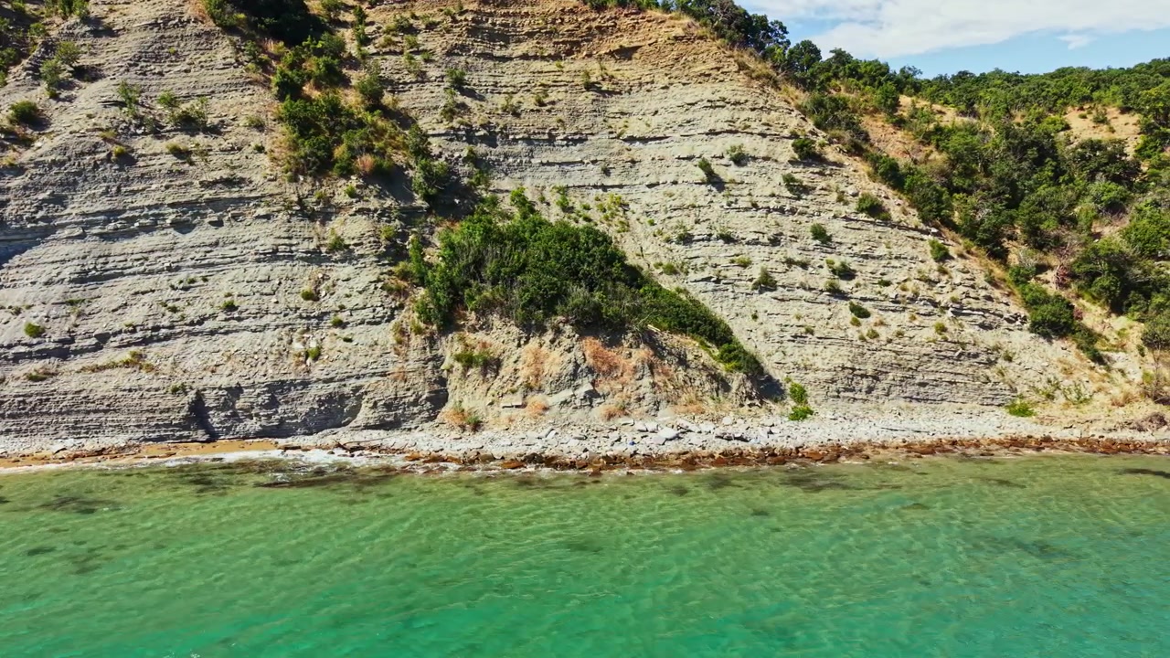 Scogliere rocciose si ergono sopra acque limpide in una zona costiera con formazioni naturali lungo la costa durante una giornata di sole.