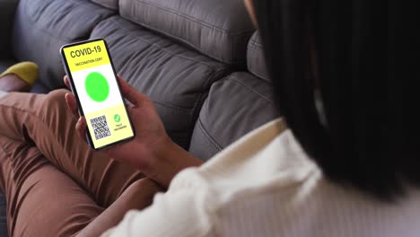 mujer en casa con un teléfono inteligente con certificado de vacunación contra la covid y código qr en la pantalla