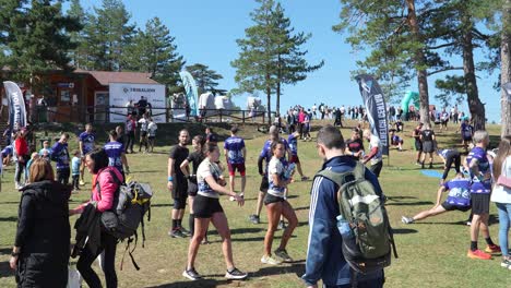 athletes are warming up and preparing for an obstacle course race at the tribalion ocr challenge, held at an outdoor location. people in the background gather near the event booths and banners.
