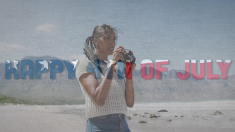 animation of text independence day over african american woman taking photo at beach