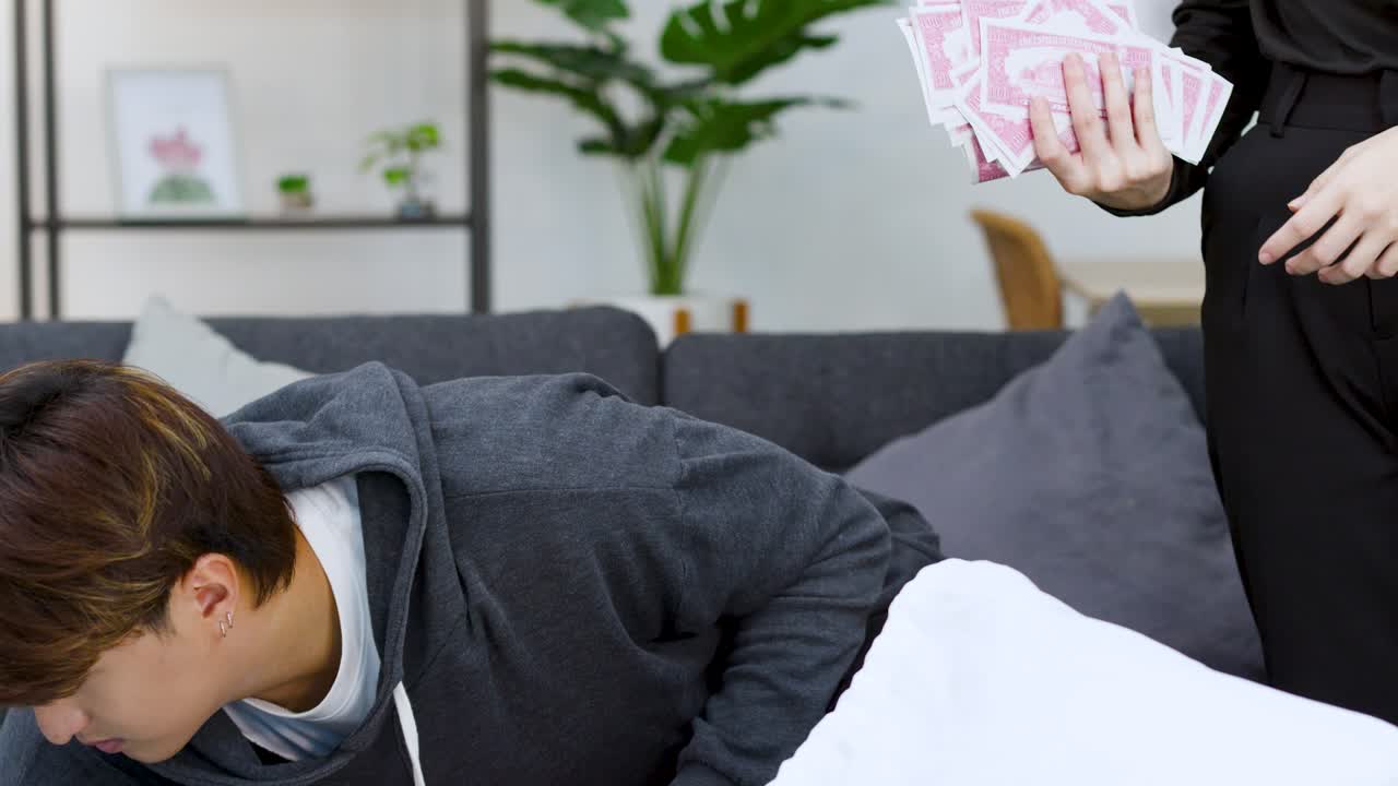 リビングルームで、パーカーを着たアジア人男性が金の延べ棒のそばで紙幣を数えている