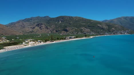 Bucht-Mit-Azurblauem-Meerwasser-An-Der-Ionischen-Küste-Albaniens,-Ruhiger-Strand-Mit-Weißem-Sand,-Grünem-Olivenhain-Und-Bergen-Im-Hintergrund